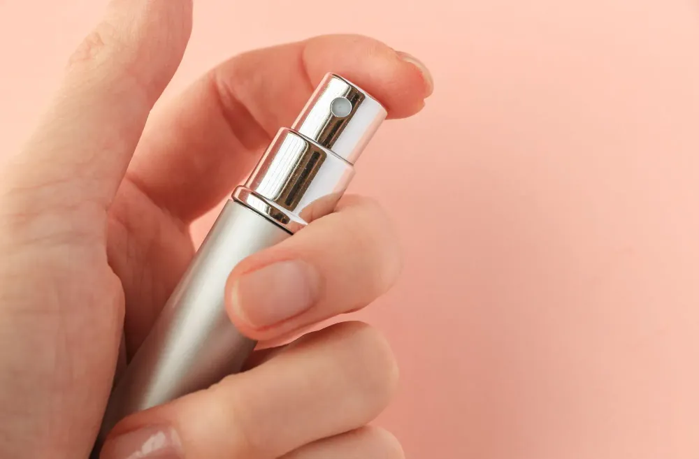 Close up of hand pressing the nozzle of a perfume atomizer on a pink backdrop